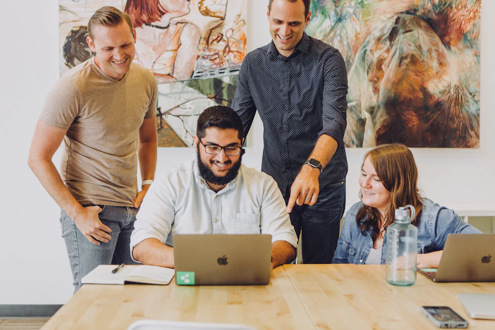 A mixed team gathered around a laptop, reviewing work together